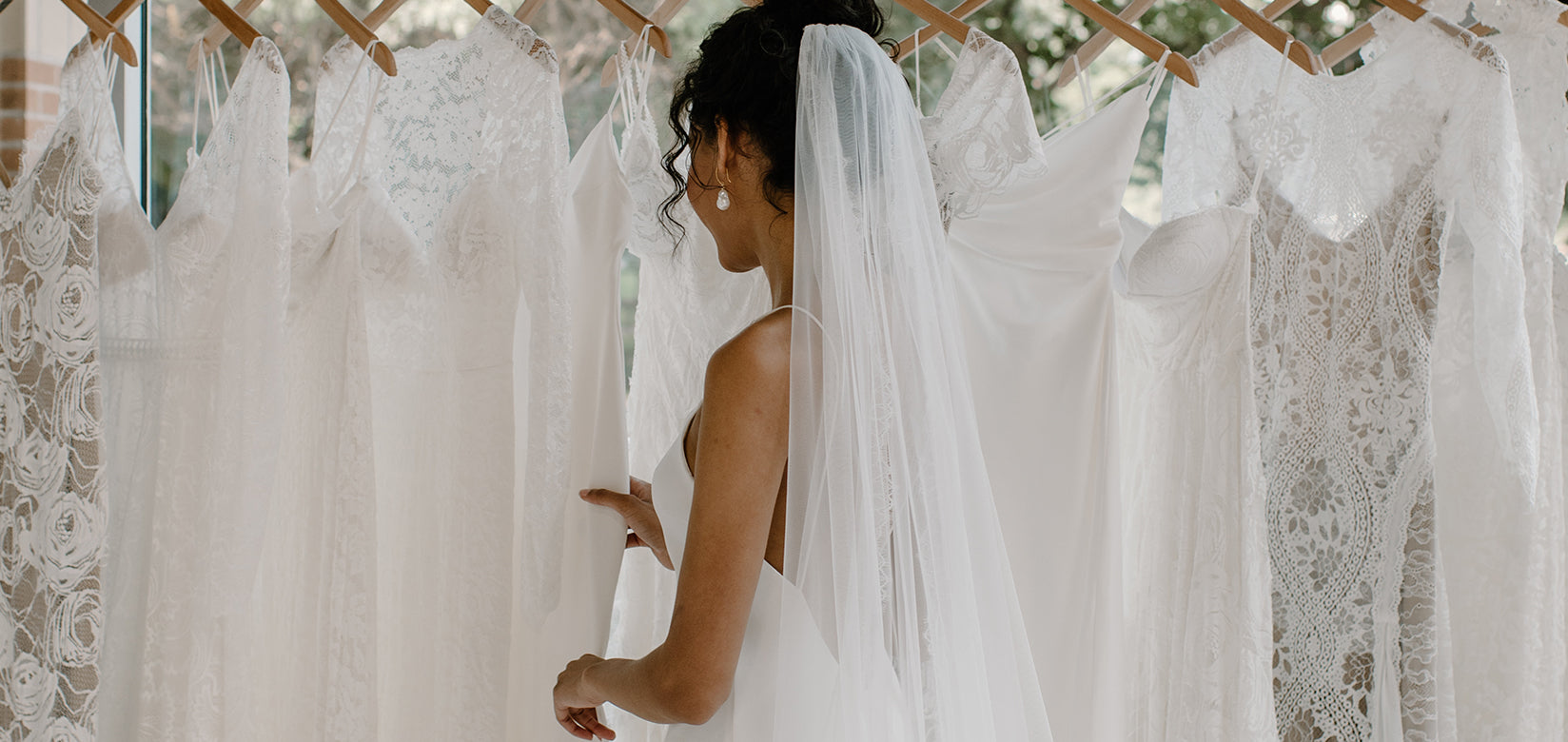 wearing wedding dress looking at wedding dresses on a rail